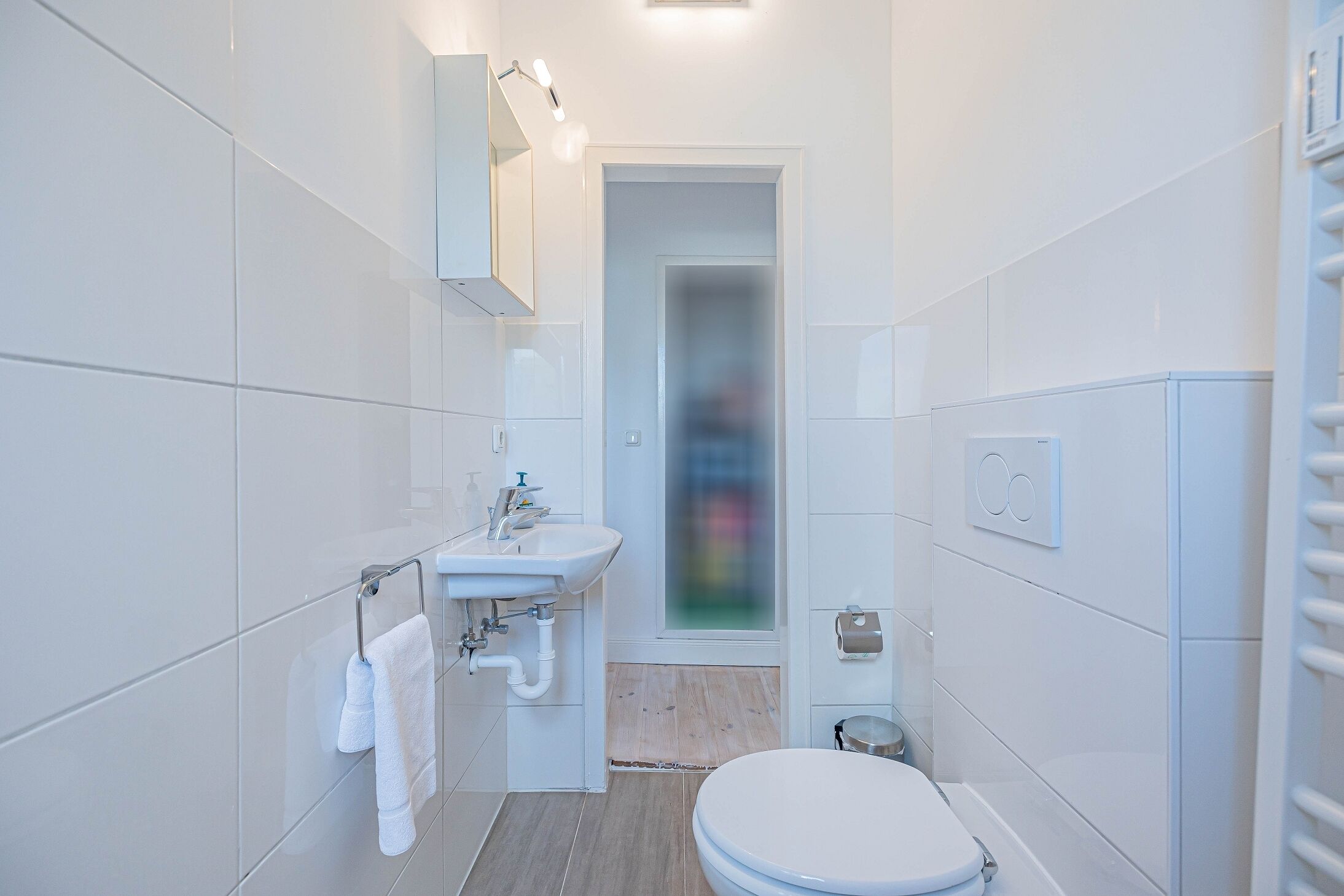 A modern bathroom with white tiles, a sink, a toilet, and a mirror.