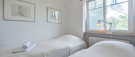 Ein Schlafzimmer mit zwei Betten, einem Fenster mit Ausblick und zwei gerahmten Kunstwerken an der Wand.