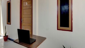 Um corredor com uma porta de madeira identificada com o número 5, um vaso de planta e um laptop sobre uma mesa de madeira.