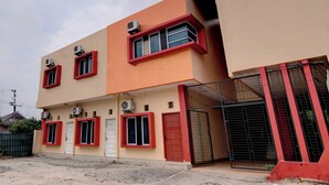 Um edifício de dois andares com várias unidades de ar condicionado, janelas com moldura vermelha e entrada com portão.