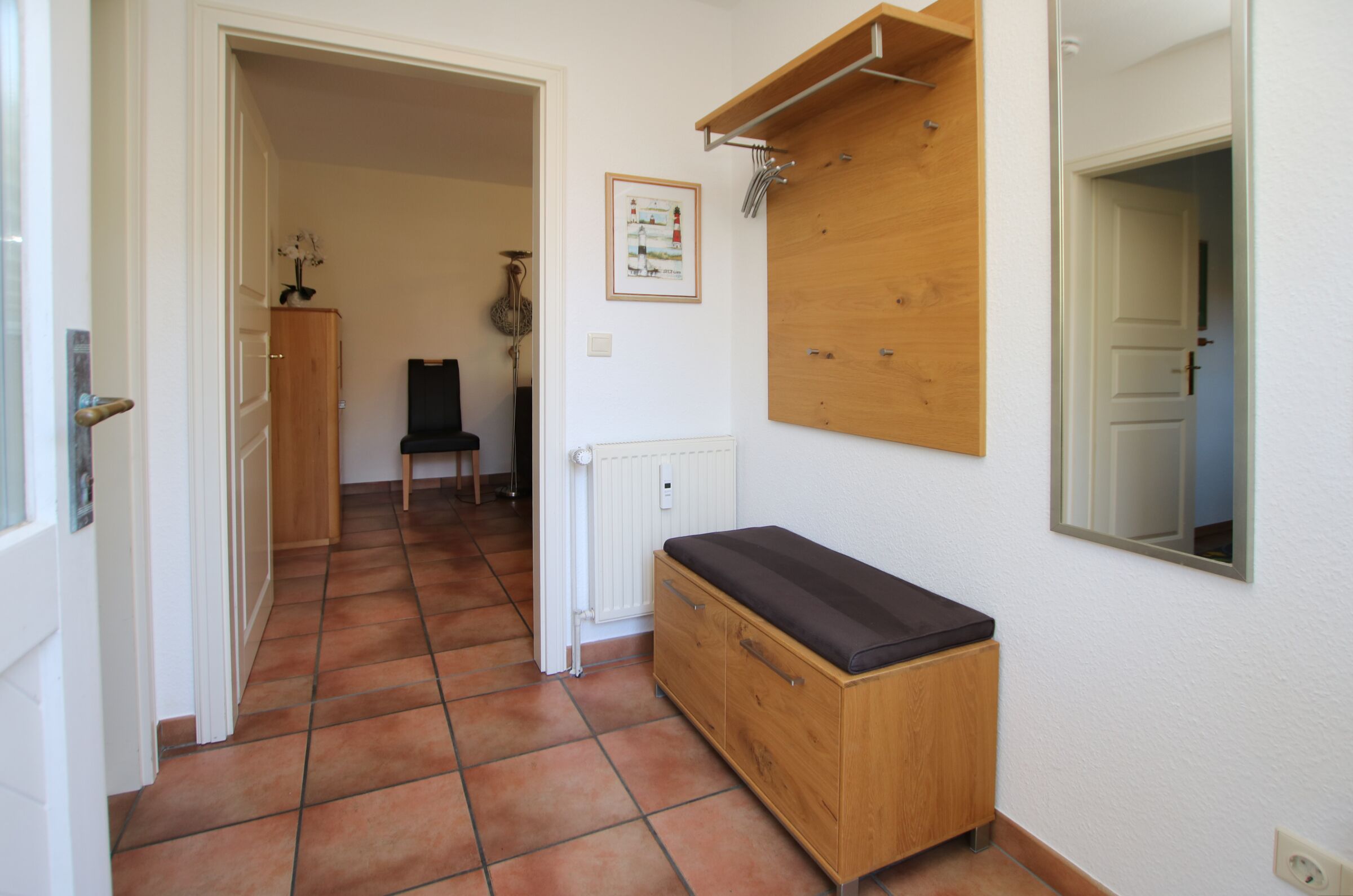 A hallway with a wooden bench, a radiator, a framed picture on the wall, and a door leading to another room.