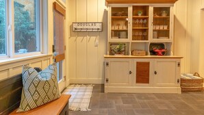 A cozy room with a wooden bench, a sign reading "DOUGLAS," and a cabinet with glass doors displaying dishes and glasses. - Your Michigan Cottage Awaits! (Douglas)