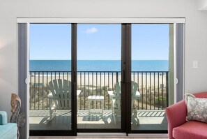 A room with a sliding glass door leading to a balcony with beach views, white chairs, and a red couch. - New! Oceanfront at Marigot Beach (Ocean City)