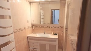 A compact bathroom with a sink, mirror, and storage cabinet. - Airy Studio with AC, Terrace, and Garage - Centrally Located in Agde (Cap d'Agde naturisme)