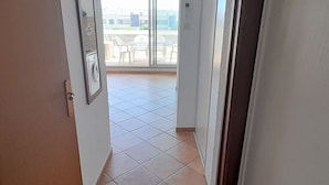 A corridor leading to a balcony with tiled flooring and a view of buildings in the distance. - Airy Studio with AC, Terrace, and Garage - Centrally Located in Agde (Cap d'Agde naturisme)