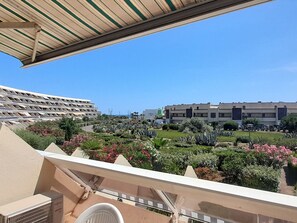 Un balcó amb vistes a un jardí paisatjístic, un edifici modern i un cel blau clar.