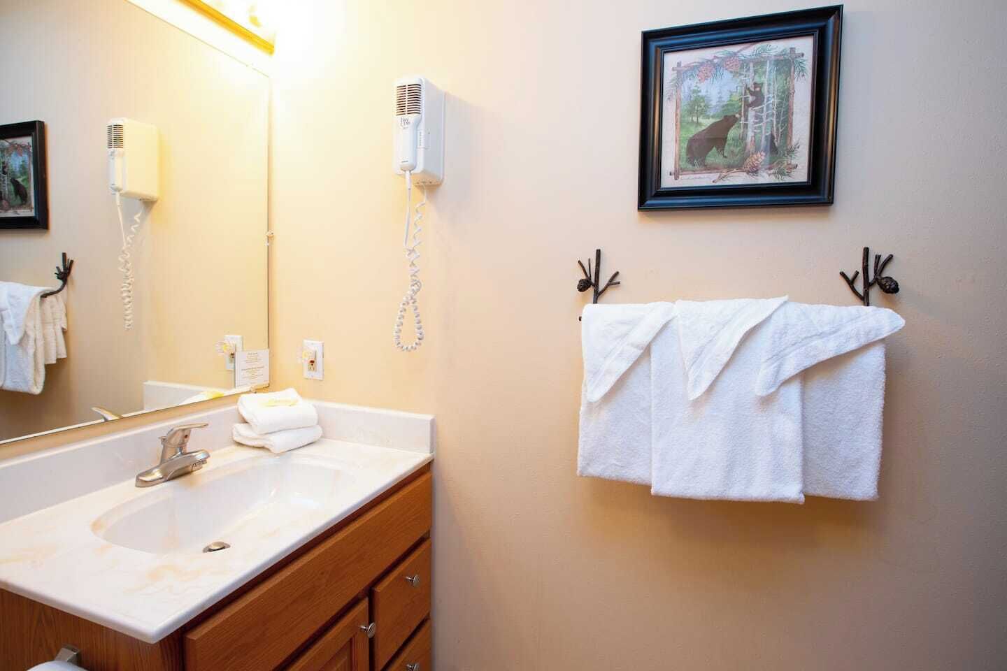 Un baño con lavamanos, espejo, perchero para toallas y un cuadro en la pared.