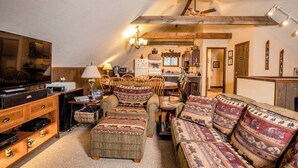Ein gemütliches Loft-Wohnzimmer mit großem Fernseher, Holzmöbeln und einer Küche im Hintergrund.