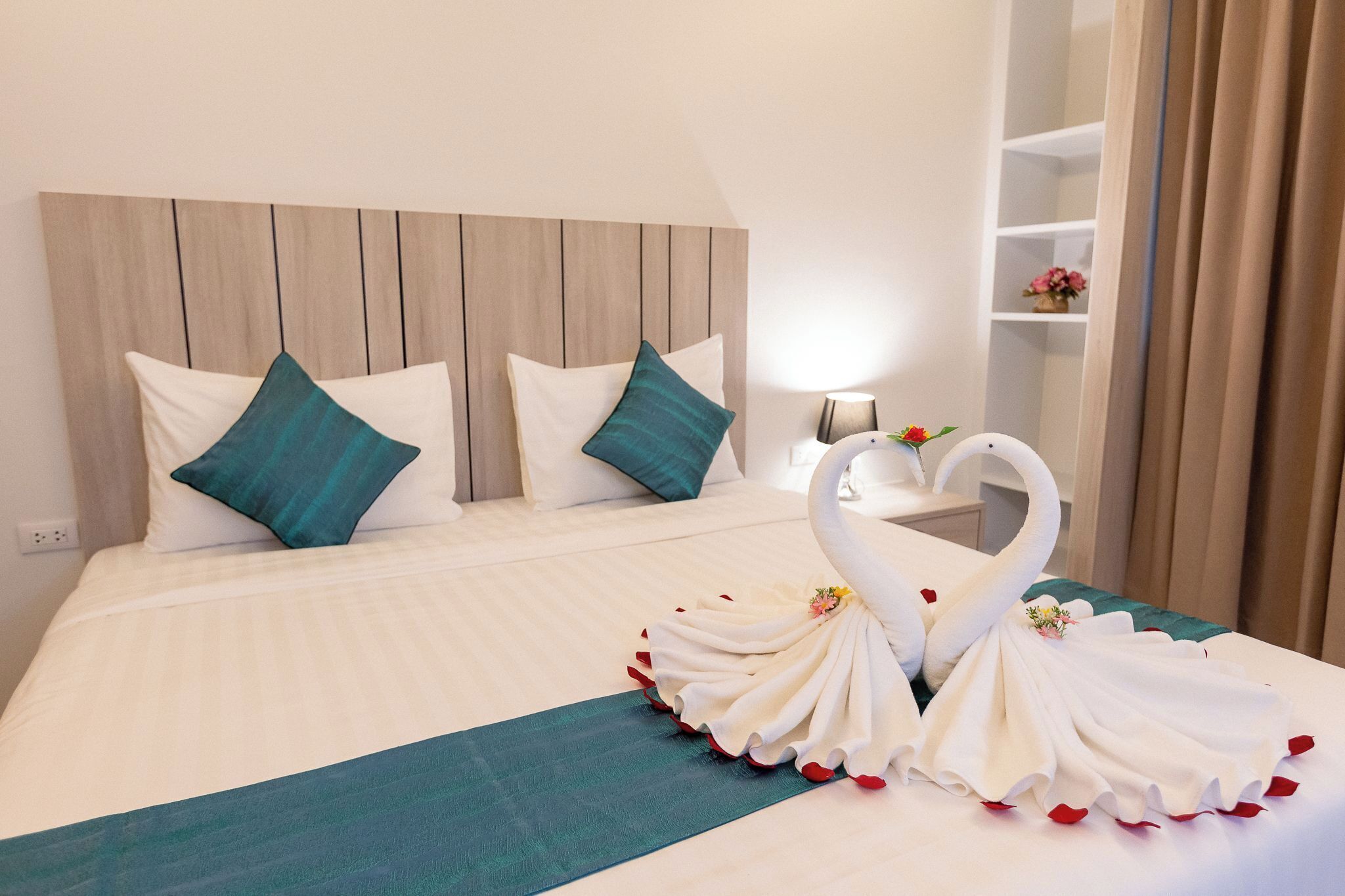 A hotel room with a bed, two pillows, a headboard, a bedside table, a lamp, and a decorative swan made of towels.