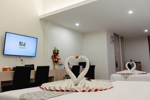 Habitación de hotel con cama, escritorio, televisor mostrando un logotipo y arreglos decorativos con forma de cisne sobre la cama.