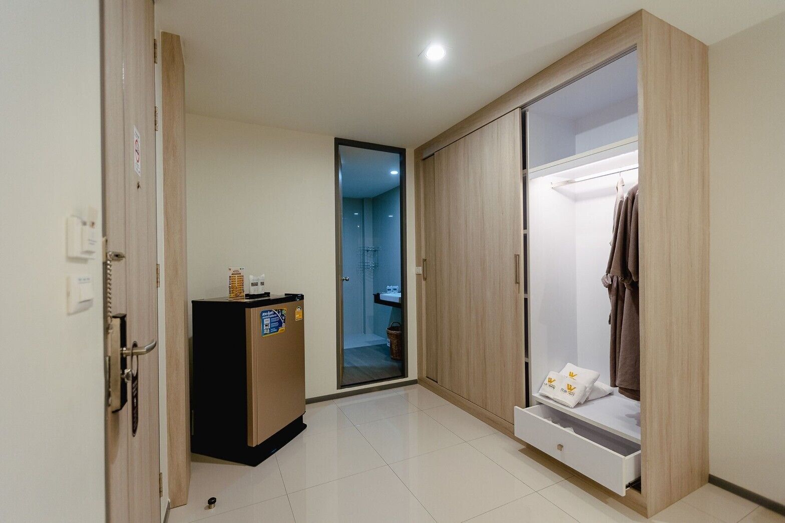 A hotel room with a wooden wardrobe, a minibar, and a bathroom visible through an open door.