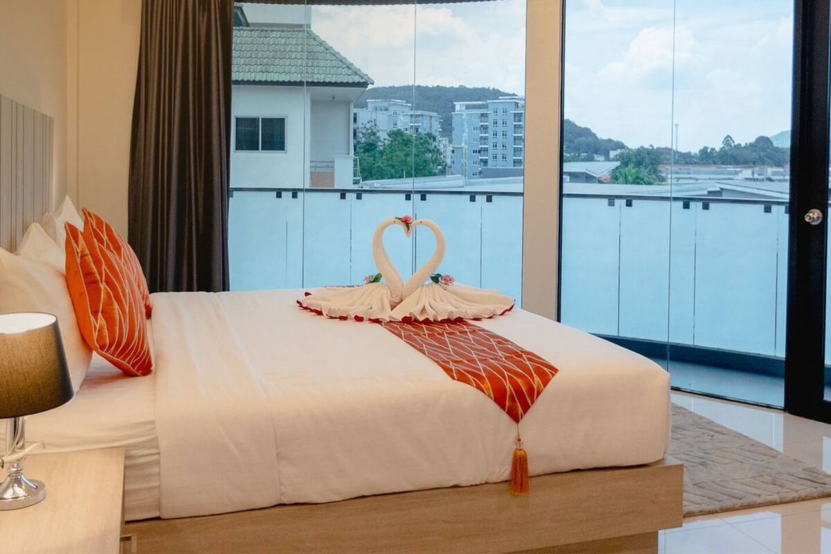A hotel room with a large bed, a bedside lamp, and a view of buildings through the window.