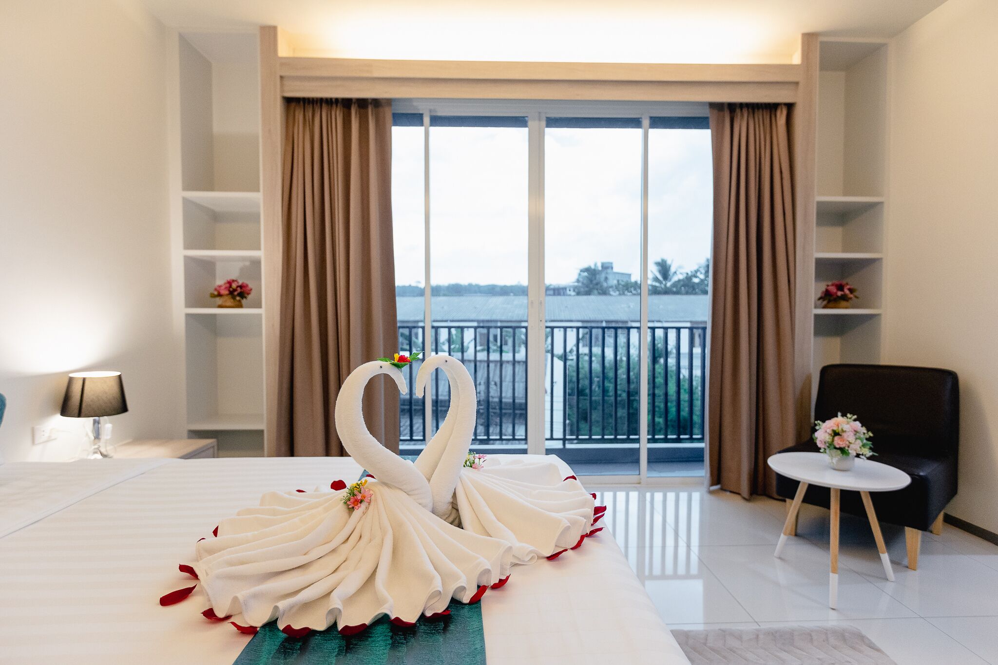 A hotel room with a bed, a chair, a table with flowers, and a view of a body of water through large windows.