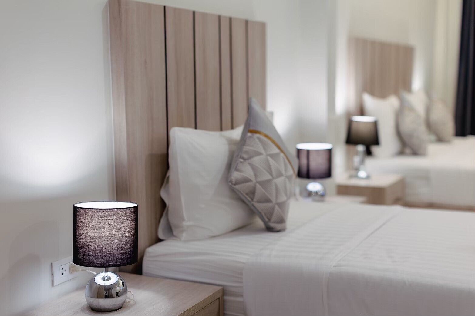 Ein Hotelzimmer mit einem hölzernen Kopfteil, einem Nachttisch mit einer Lampe und einem Bett mit einem Kissen.