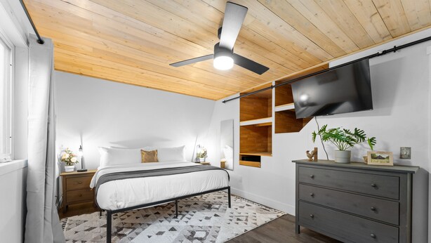 A bedroom with a bed, a dresser, a ceiling fan, a TV, and a window with curtains.