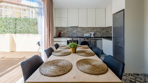 A modern kitchen with white cabinets, a stainless steel refrigerator, and a dining area with a wooden table and black chairs.