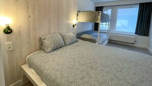 Una camera da letto con un letto a castello, un letto grande con biancheria a motivi, una parete in legno e una finestra con tende.