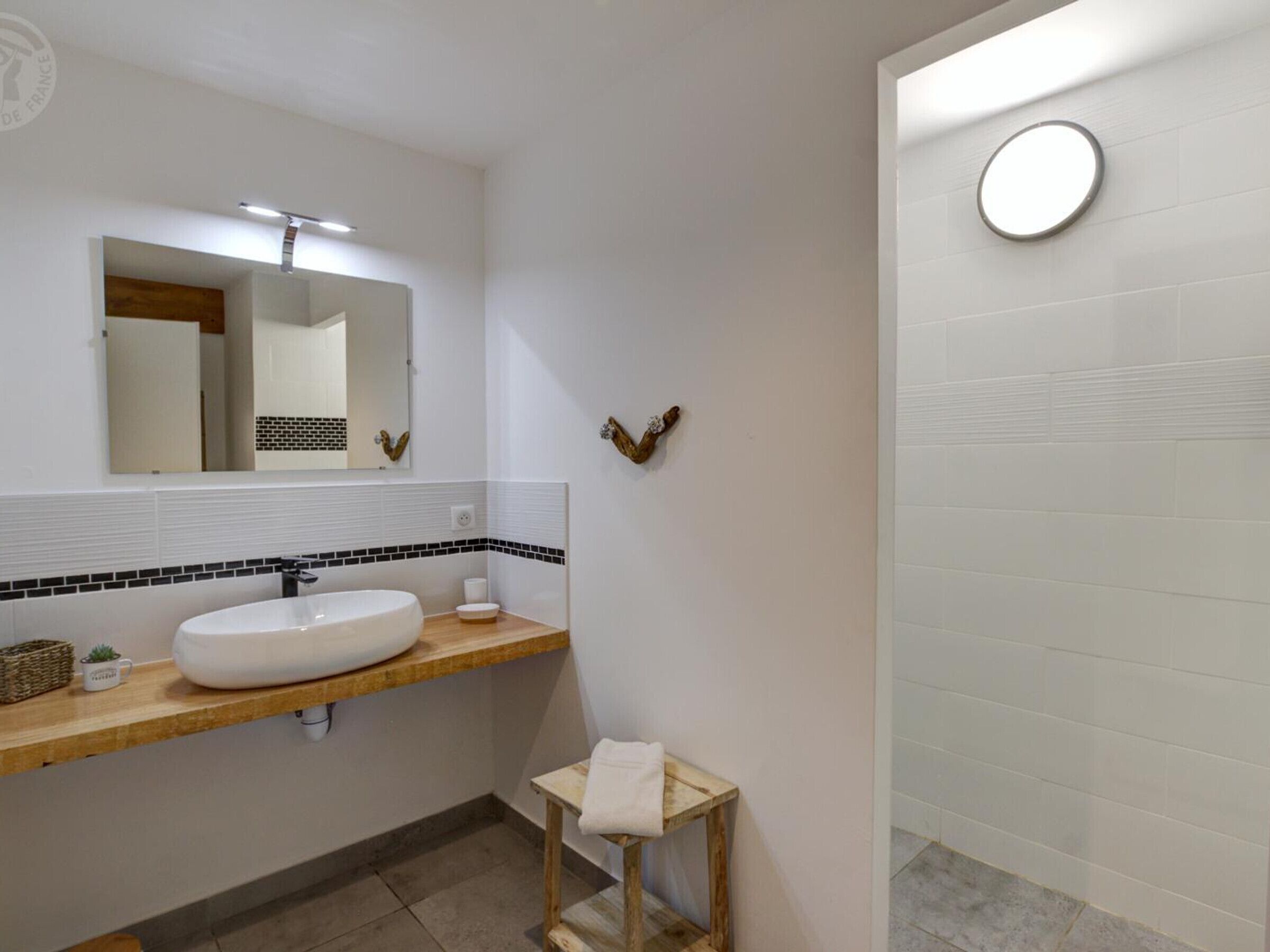 A modern bathroom with a white sink, a mirror, and a small wooden stool.