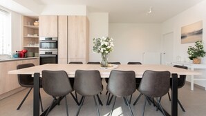 A modern kitchen with a central island, built-in appliances, and a dining area with a long table and chairs. - Villa Petit Mousse -Luxurious villa close to beach (Koksijde)