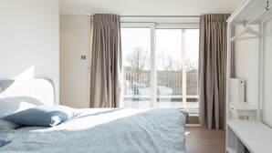 A bedroom with a bed, a bench, a window with curtains, and a view of the outside. - Villa Petit Mousse -Luxurious villa close to beach (Koksijde)