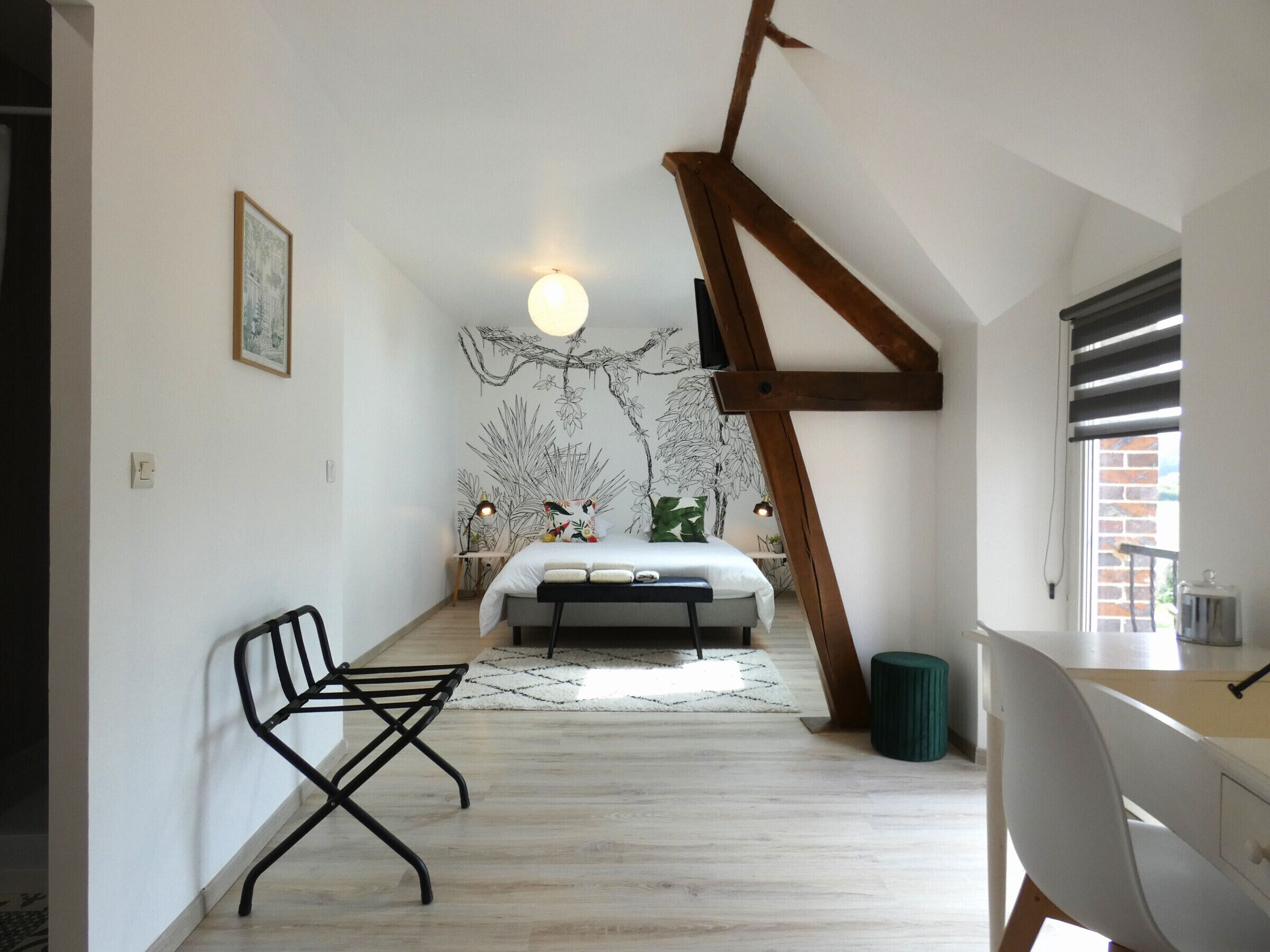 Ein Schlafzimmer mit schrägem Dach, einem Bett, einem Schreibtisch, einem Stuhl und einer Wand mit einer Baummalerei.