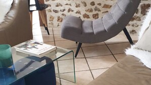 Una sala de estar con una mesa de centro de vidrio, un sillón gris y un sofá color crema.
