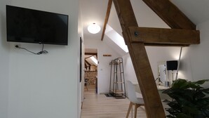 Un interior moderno con estructura de vigas de madera, un televisor de pantalla plana montado en la pared, una silla blanca y una planta en maceta.
