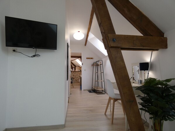 Un interior moderno con estructura de vigas de madera, un televisor de pantalla plana montado en la pared, una silla blanca y una planta en maceta.