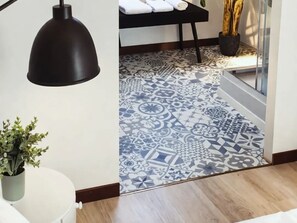 Een kamer met een patroon vloer, een potplant, een hanglamp en een bed met opgevouwen handdoeken.