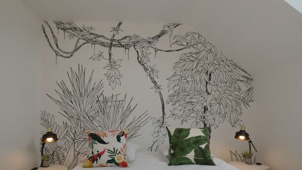Un dormitorio con una cama, dos mesitas de noche con lámparas y un mural en la pared con un árbol y follaje.