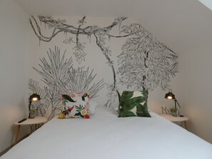 Quarto com cama, duas mesas de cabeceira com luminárias e um mural na parede retratando uma árvore e folhagem.