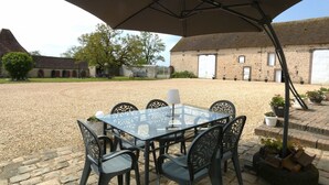 Una mesa con sillas y un paraguas grande en un patio con un edificio al fondo.