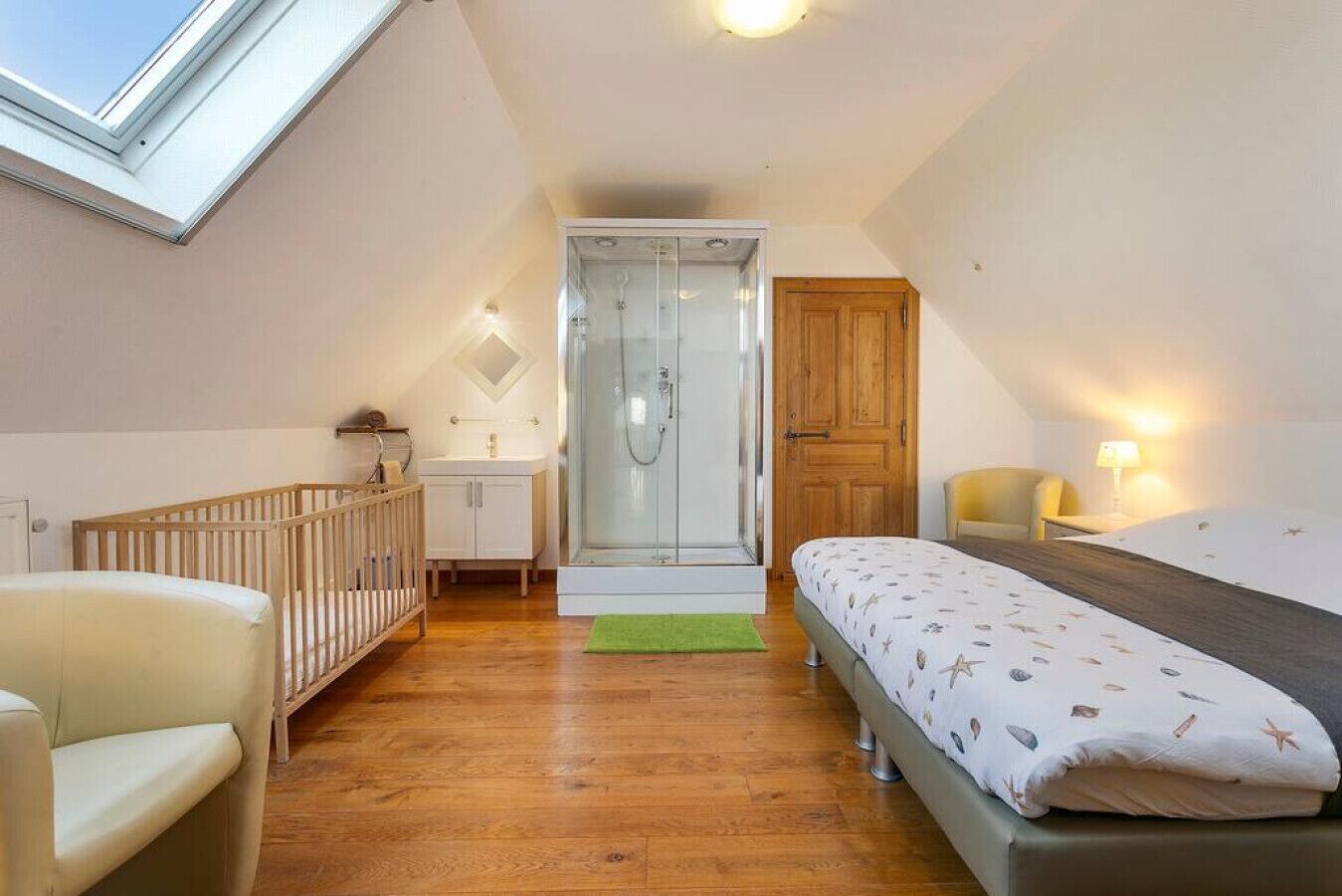 Une chambre avec un puits de lumière, une douche, un berceau, un lit et une petite salle de bain.