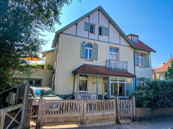 A two-story building with a balcony on the second floor, a covered entrance, and a wooden fence in front. - Villa Trianon -Summer beachhouse in De Panne (De Panne)