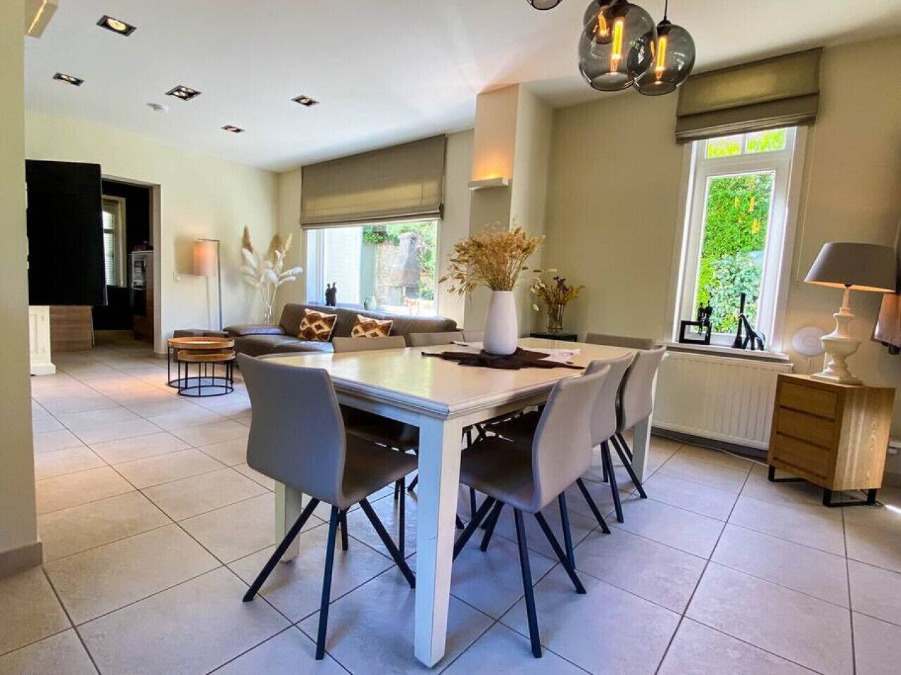 Een moderne eetruimte met een witte tafel, grijze stoelen en een kroonluchter.