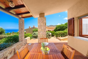 Un patio con una mesa y sillas de madera, un cuenco de fruta y vistas al mar y a las montañas.