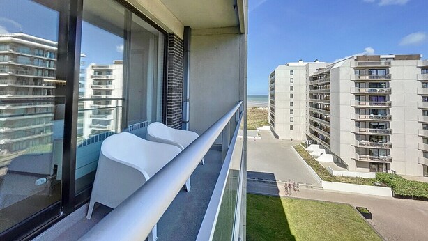 Ein Balkon mit zwei weißen Stühlen, einer Glastrennwand und Blick auf angrenzende Hochhäuser.