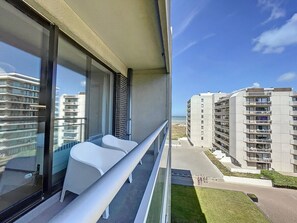 Un balcon avec deux chaises blanches, une balustrade en verre et une vue sur les immeubles de grande hauteur situés à proximité.