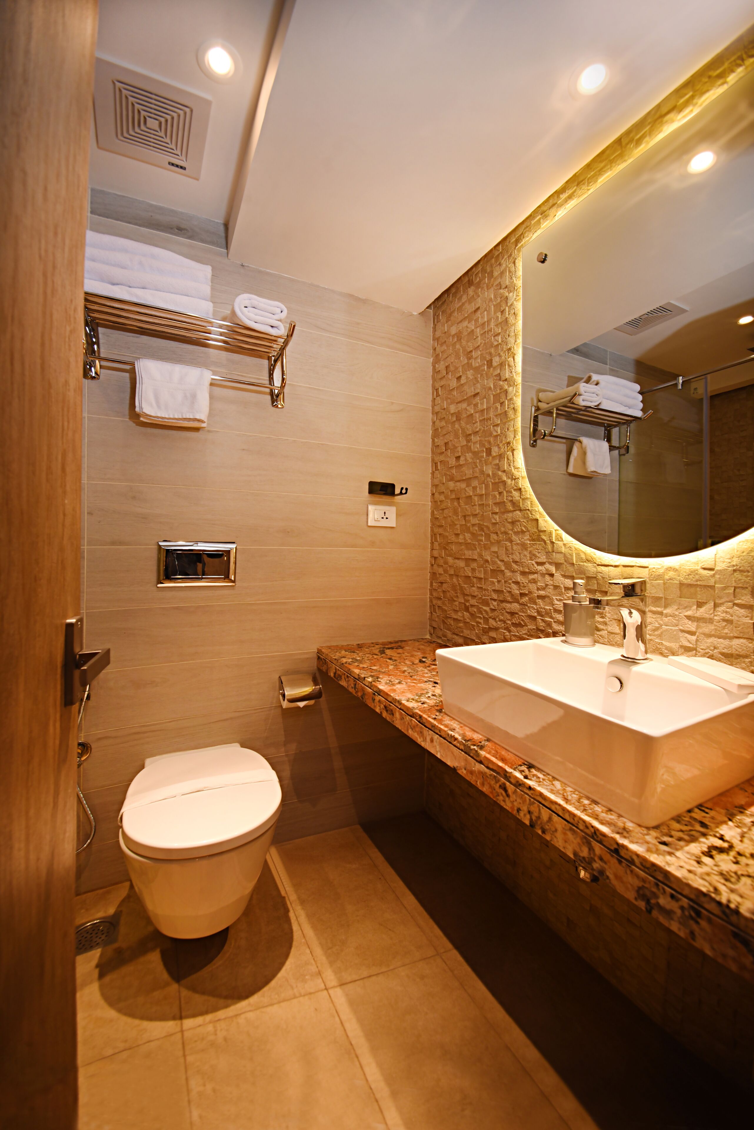 A modern bathroom with a marble countertop, a large mirror, and a toilet.