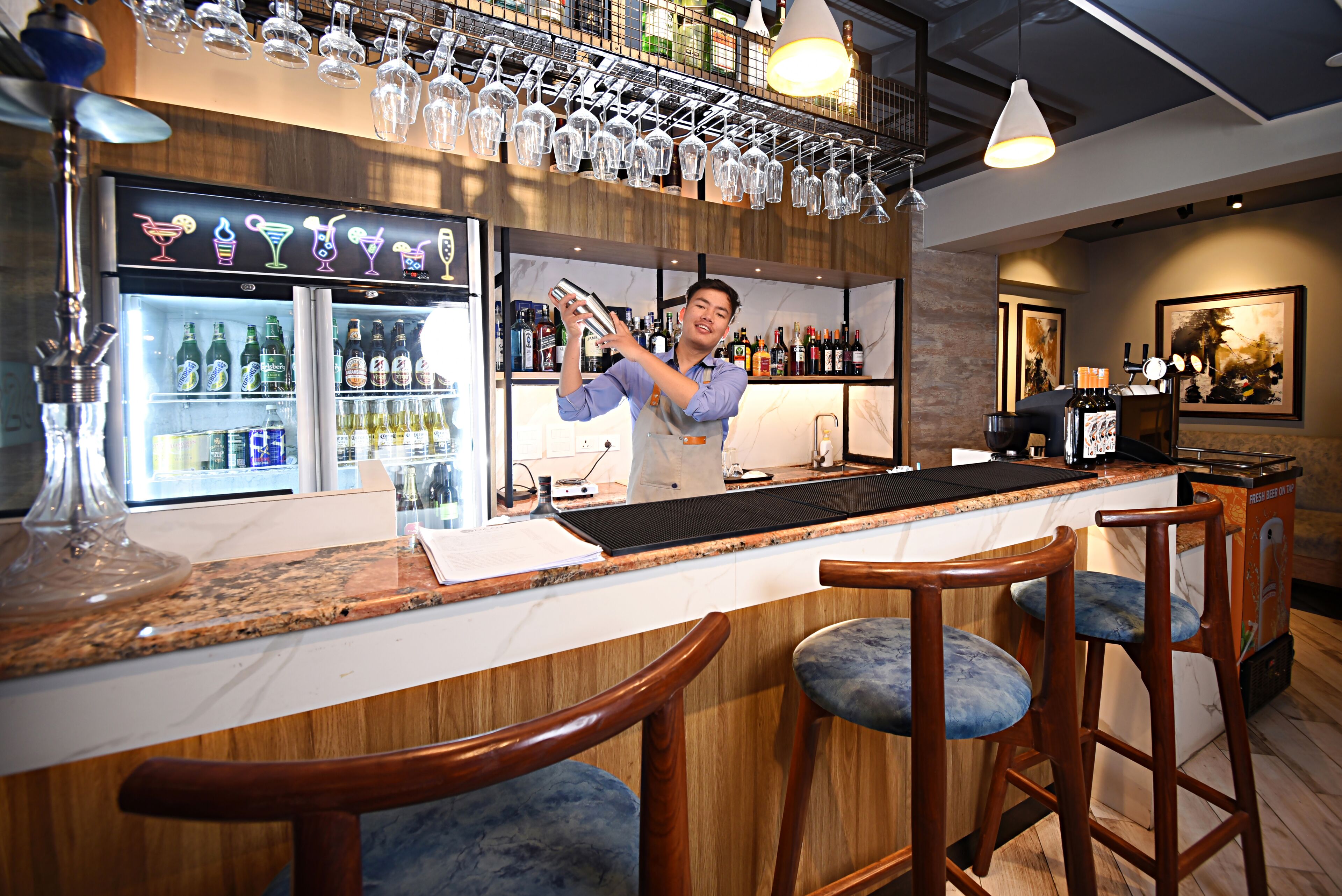 Zona de bar con un barman, un refrigerador bien surtido y una variedad de botellas.