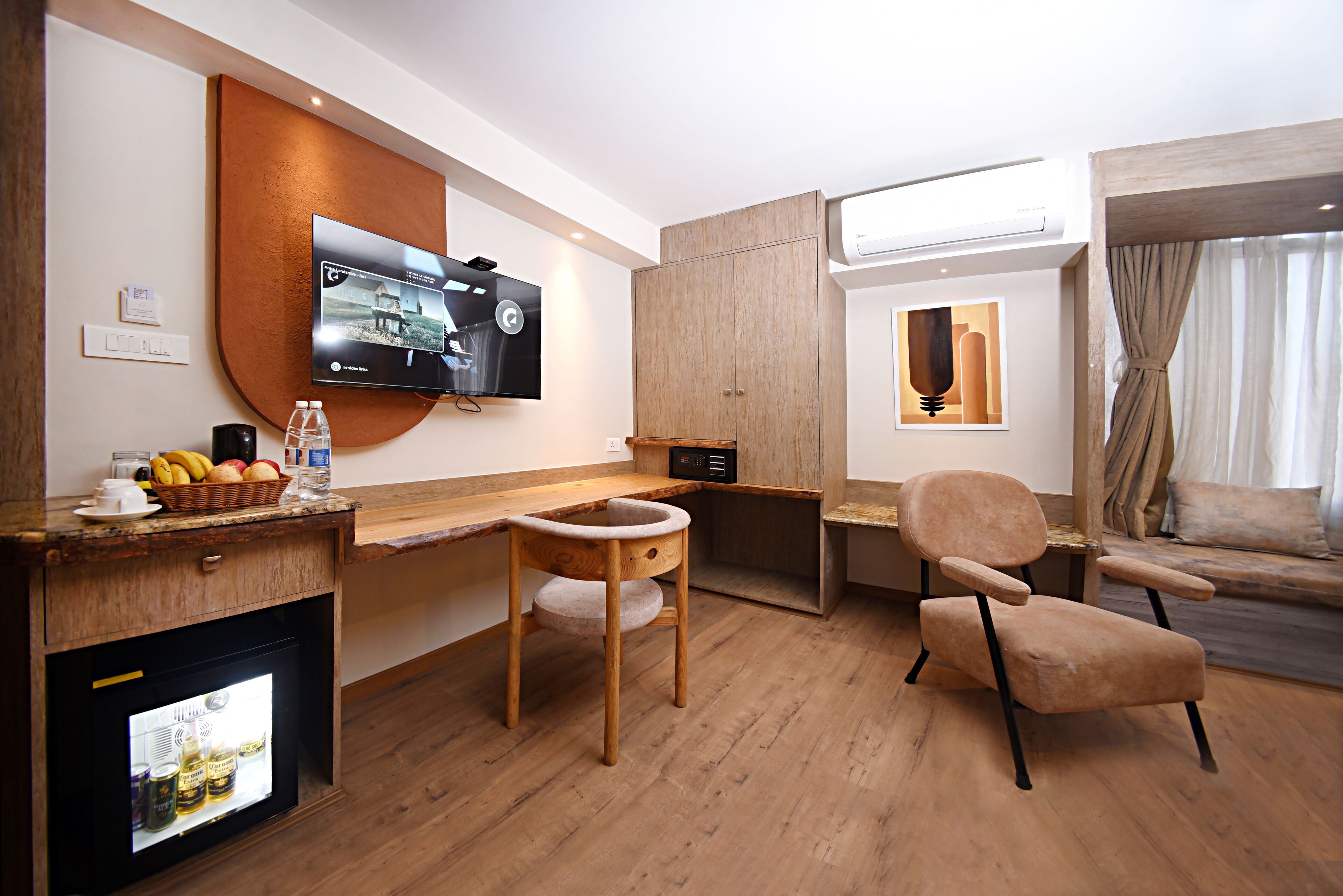 Una habitación de hotel moderna con un escritorio de madera, un sillón cómodo, un televisor montado en la pared y un mini refrigerador integrado.