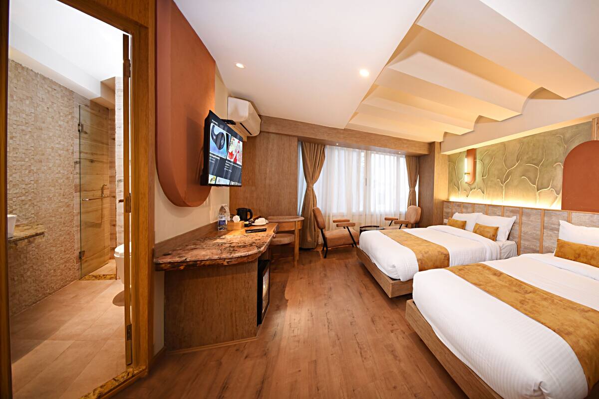 A hotel room with two beds, a desk, a TV, and a shower area.