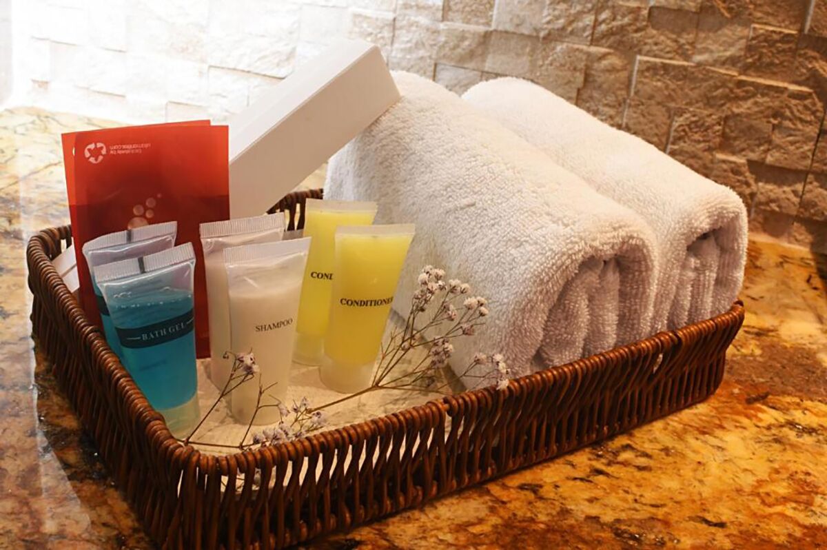 A wicker basket containing toiletries, towels, and a card on a marble countertop.