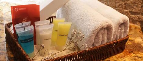 A wicker basket containing toiletries, towels, and a card on a marble countertop.