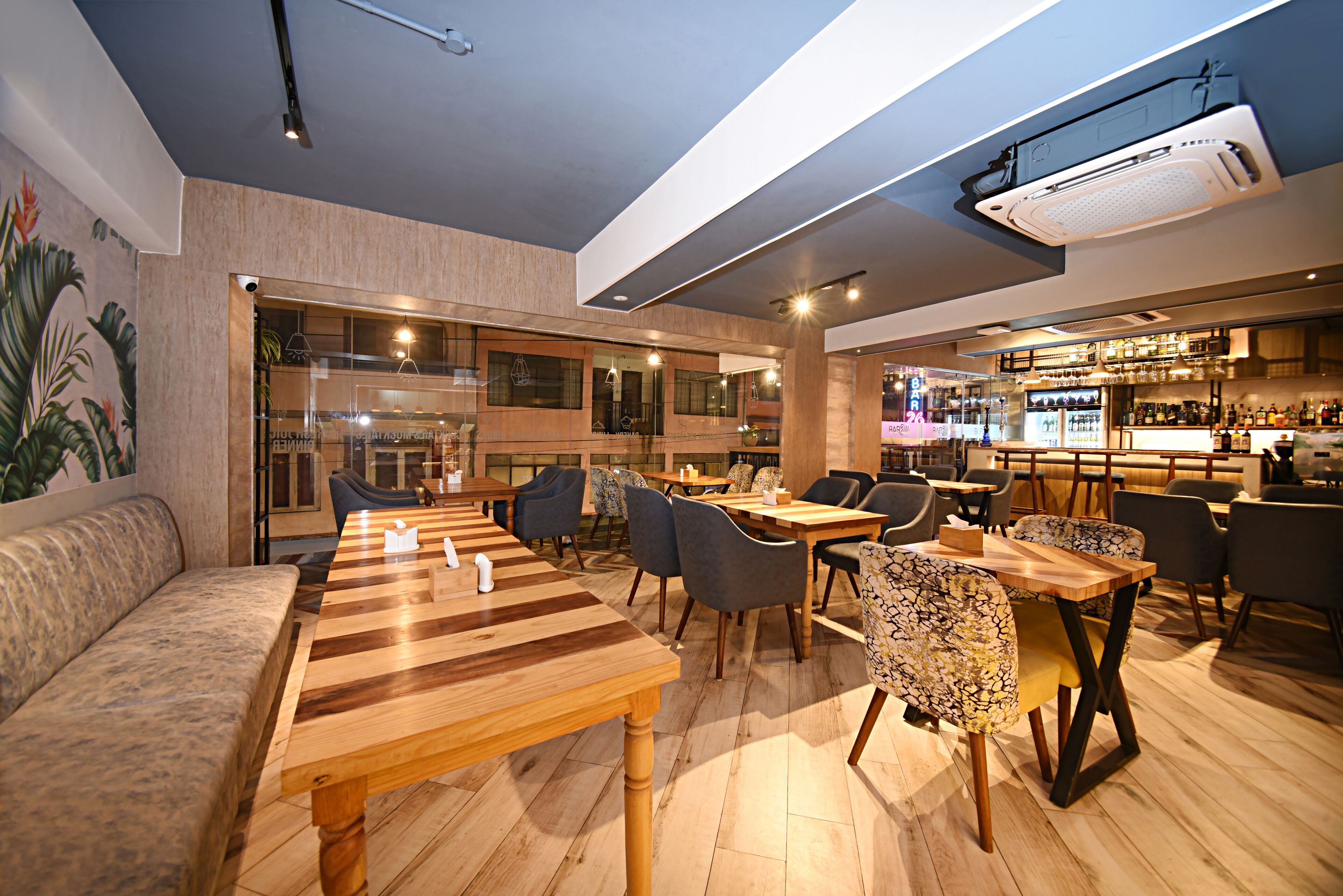 A modern restaurant with wooden tables and chairs, a bar area, and a seating area with a cushioned bench.