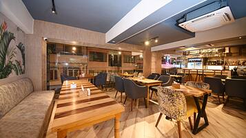 A modern restaurant with wooden tables and chairs, a bar area, and a seating area with a cushioned bench.