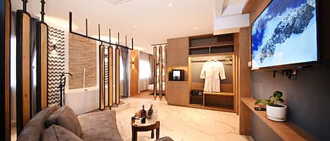 A modern hotel lobby with a sofa, a TV screen, a coat rack, and a potted plant.