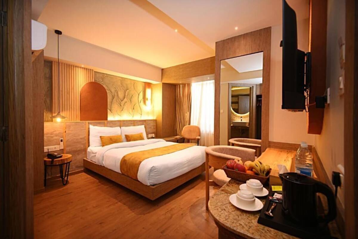 A hotel room with a large bed, a sitting area with a chair and a small table, a mirror, and a fruit basket.