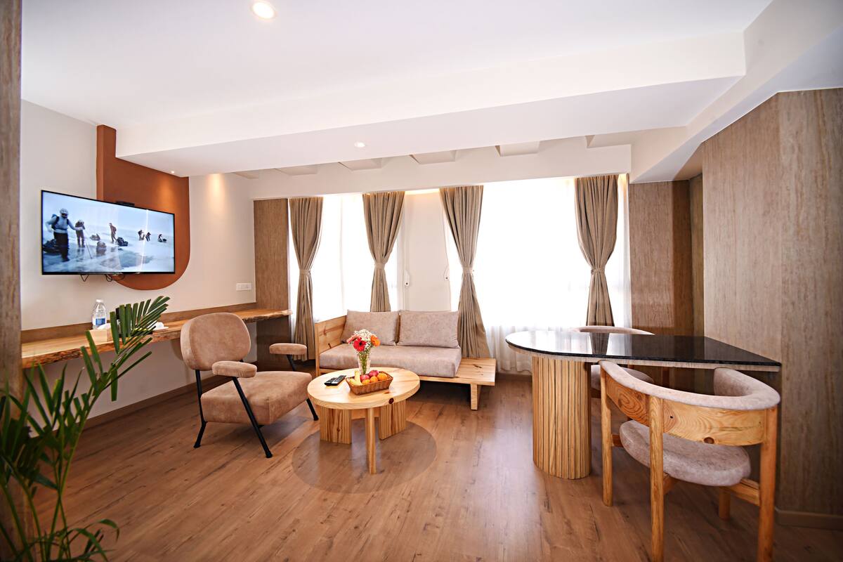 A modern living room with a flat-screen TV, wooden furniture, a sofa, and a dining area with a glass table.