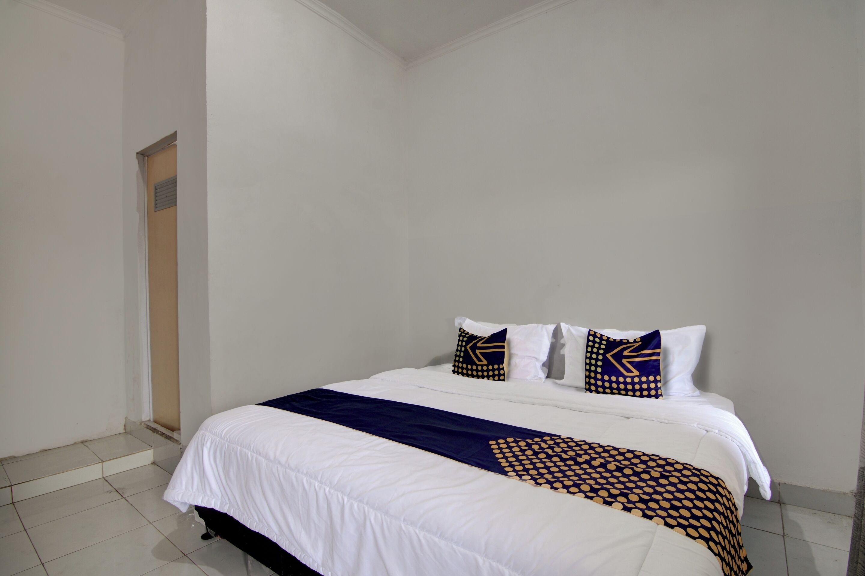 A hotel room with a large bed, white bedding, and decorative pillows with geometric patterns.